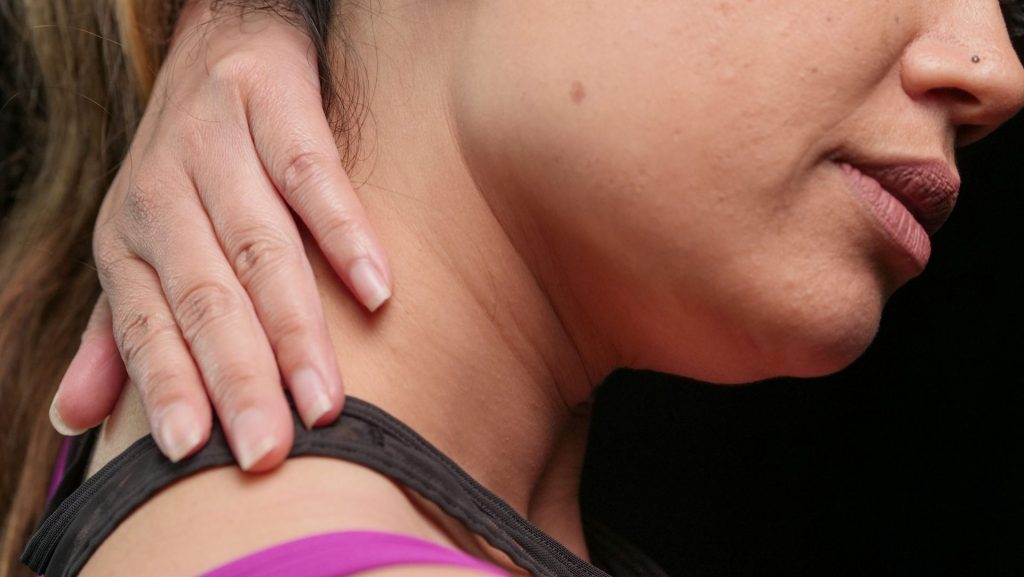 Close-up of a woman holding her neck, indicating pain or discomfort.